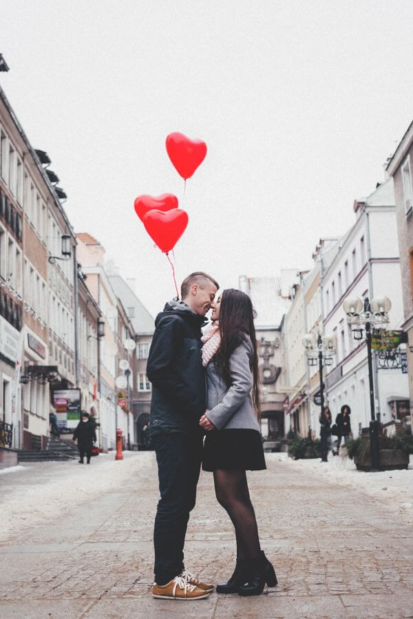 Couple embracing in a street holding heart balloons